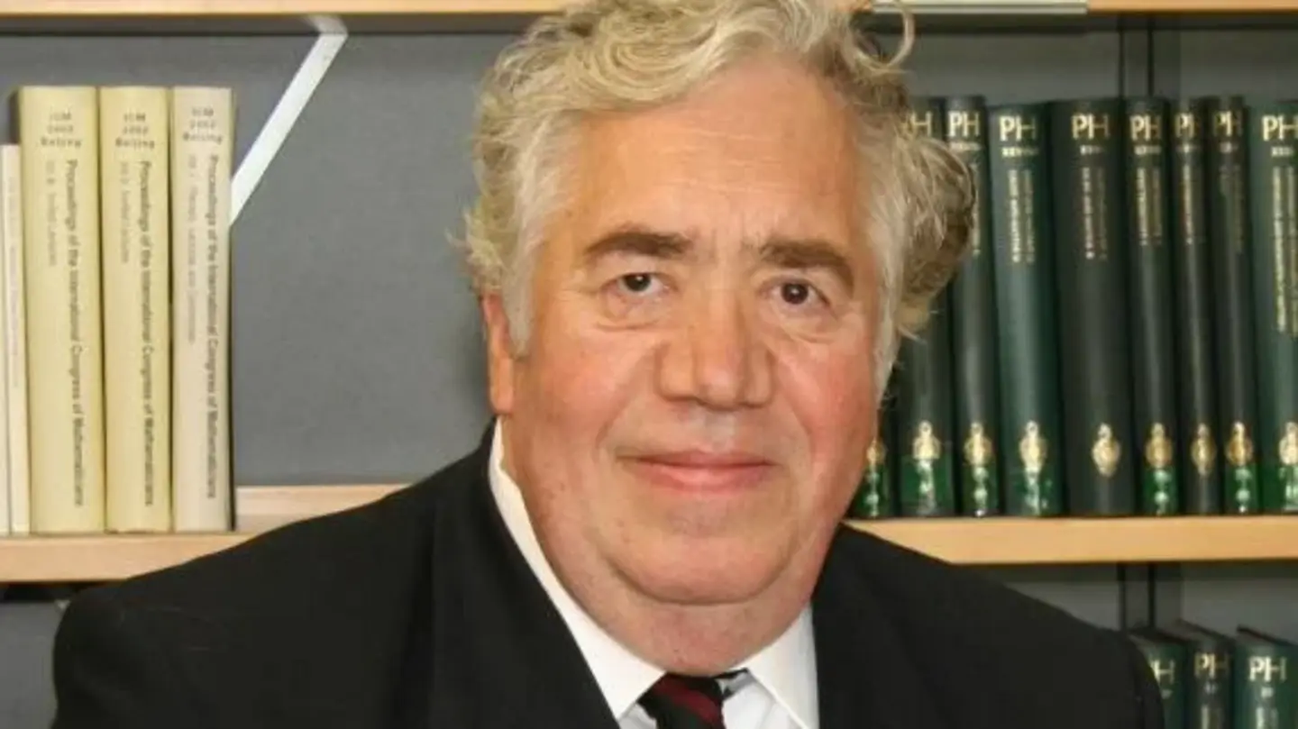 Portrait of Eberhard Zeidler giving a speech in front of some bookshelves in the library