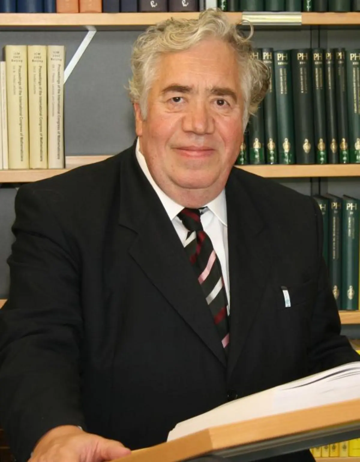 Portrait of Eberhard Zeidler giving a speech in front of some bookshelves in the library