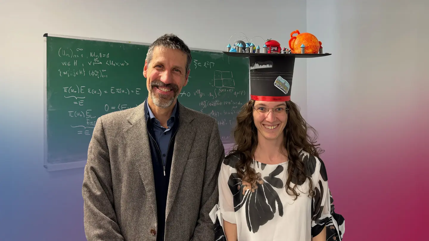 László Székelyhidi and Sandra Ried smile in front of a blackboard