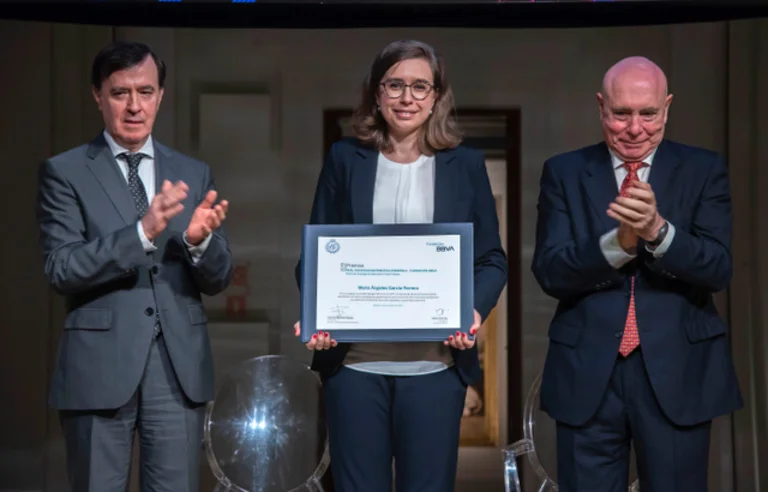 María Ángeles García-Ferrero holds the award certificate. Next to her are two men who are applauding her.