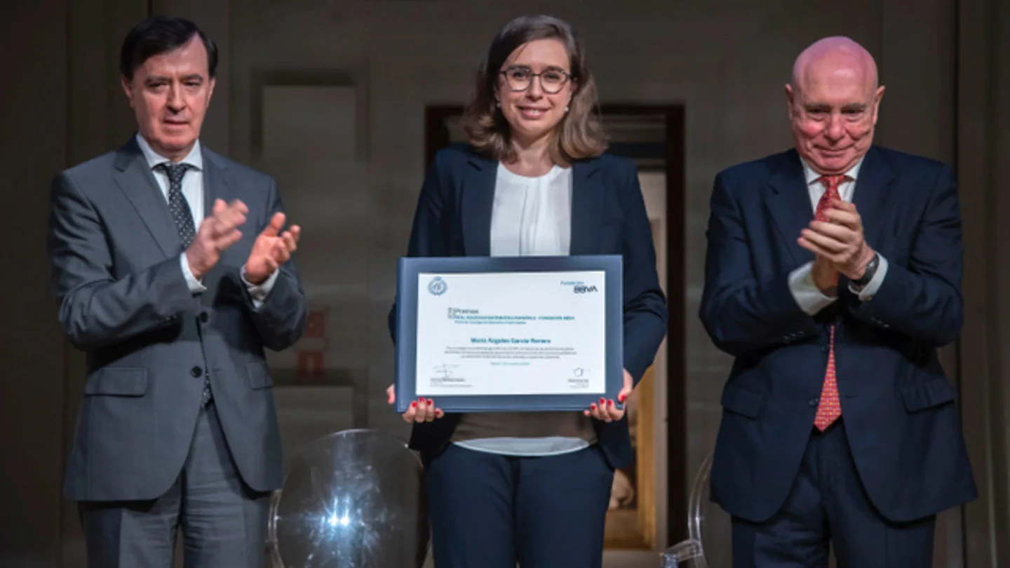 María Ángeles García-Ferrero holds the award certificate. Next to her are two men who are applauding her.