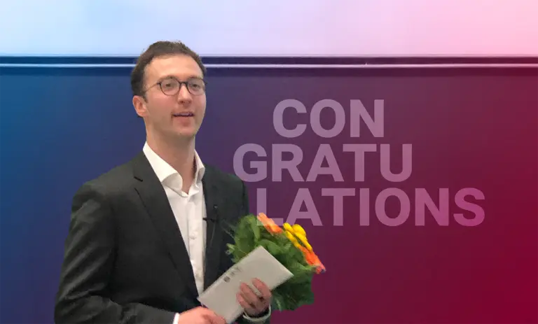 Giulio Zucal after he finished his dissertation, standing in front of a blackboard with a bunch of flowers and a document in his hands