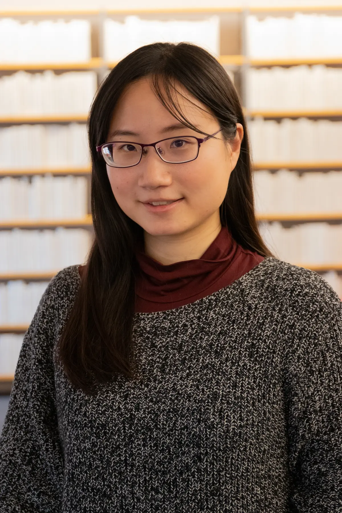 Porträt von Enya Hsiao vor einer weißen Bücherwand