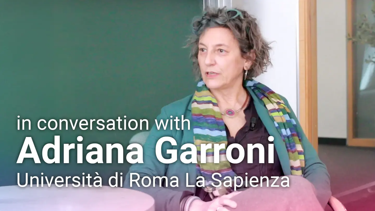 Adriana Garroni from the Universitá di Roma La Sapienza sits in front of a blackboard and gives an interview for the video format “in conversation with.”