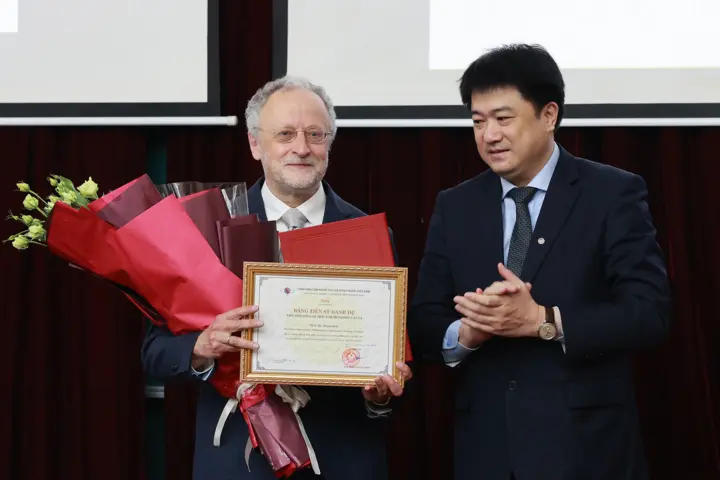 Jürgen Jost with a bouquet of flowers and a certificate in his hands, next to him a Vietnamese colleague