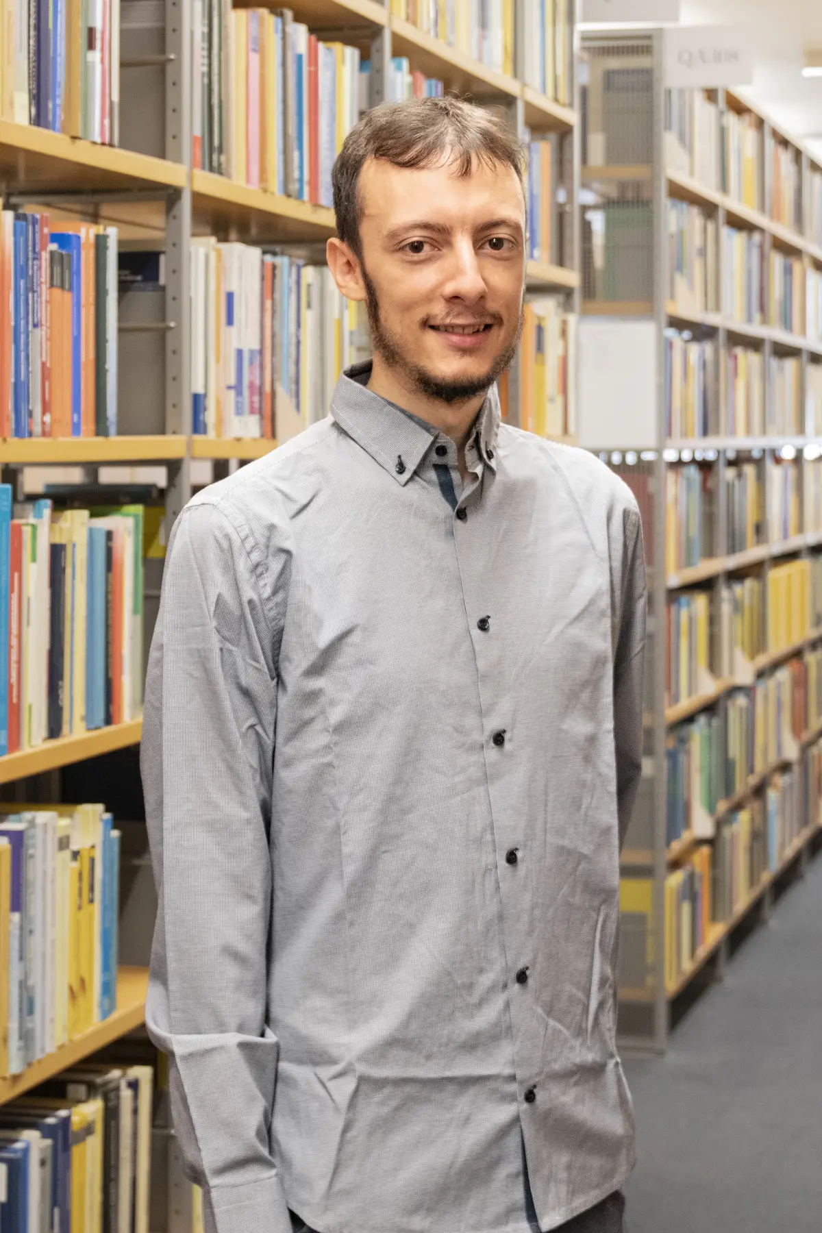 Porträt von Alessio Borzi vor einem Bücherregal, einen Arm hinter dem Rücken