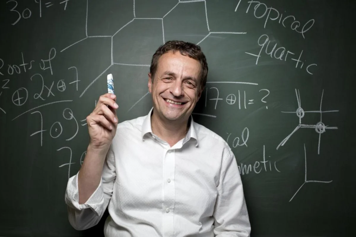 Portrait of Bernd Sturmfels, a blackboard with mathematical formulas in the background