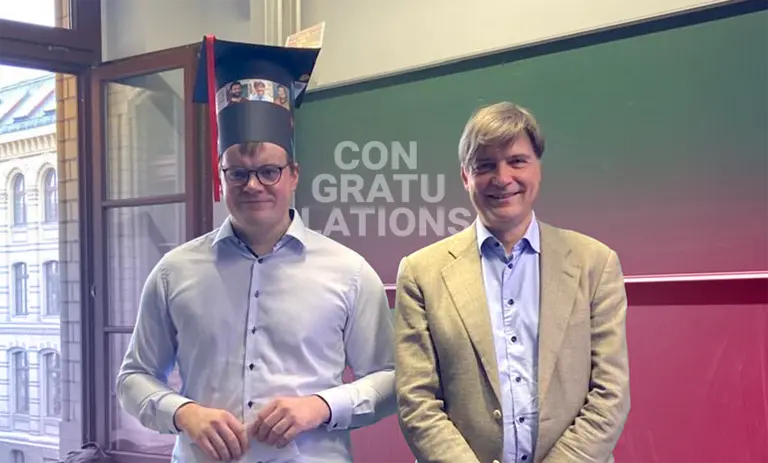 Christian Wagner and Felix Otto are standing in front of a blackboard and smiling; the text “Congratulations” in the background is visible