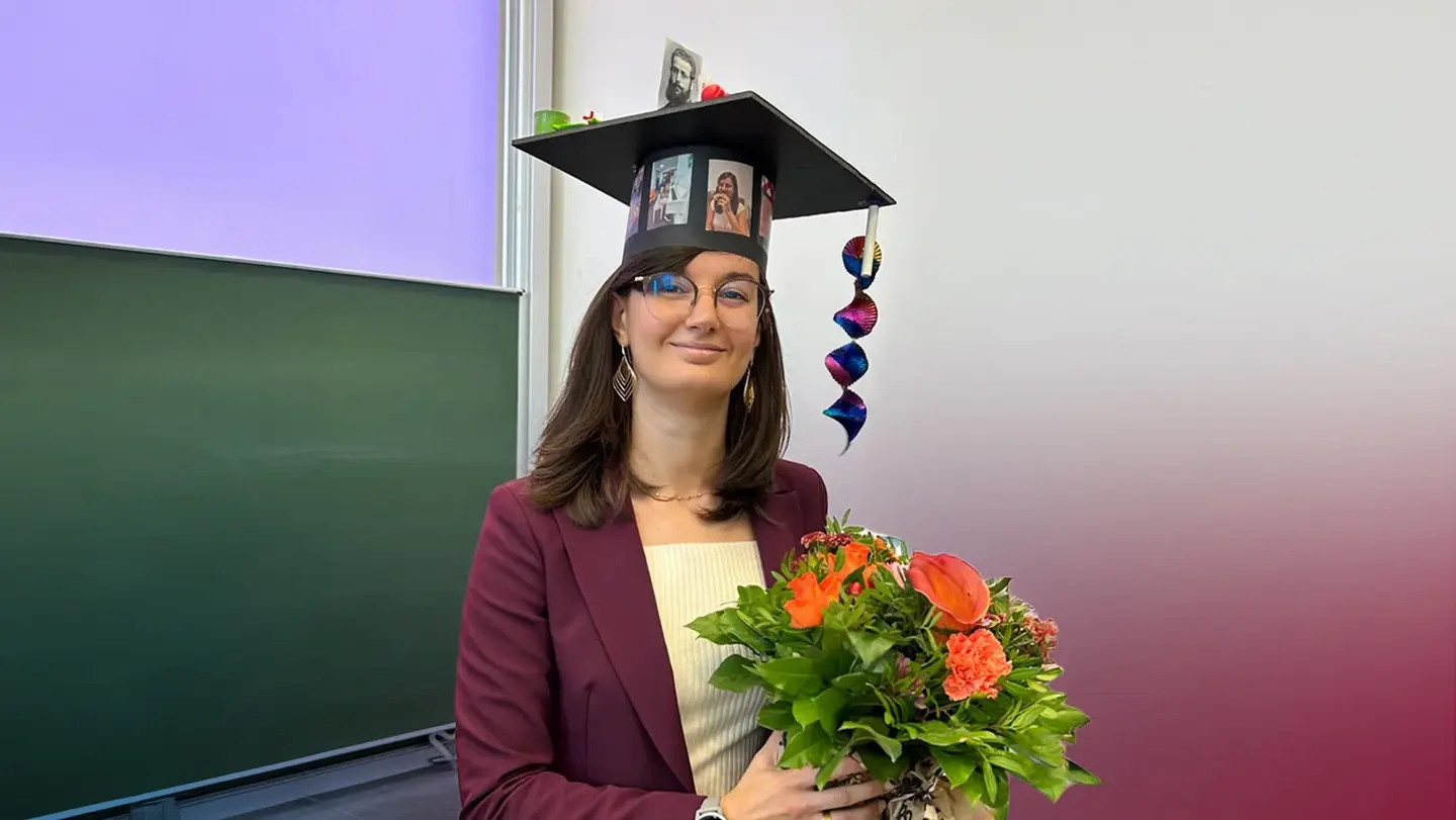 Betti Barbara smiles into the camera. She is holding a flower bouquet in her hands and wearing a graduation hat.
